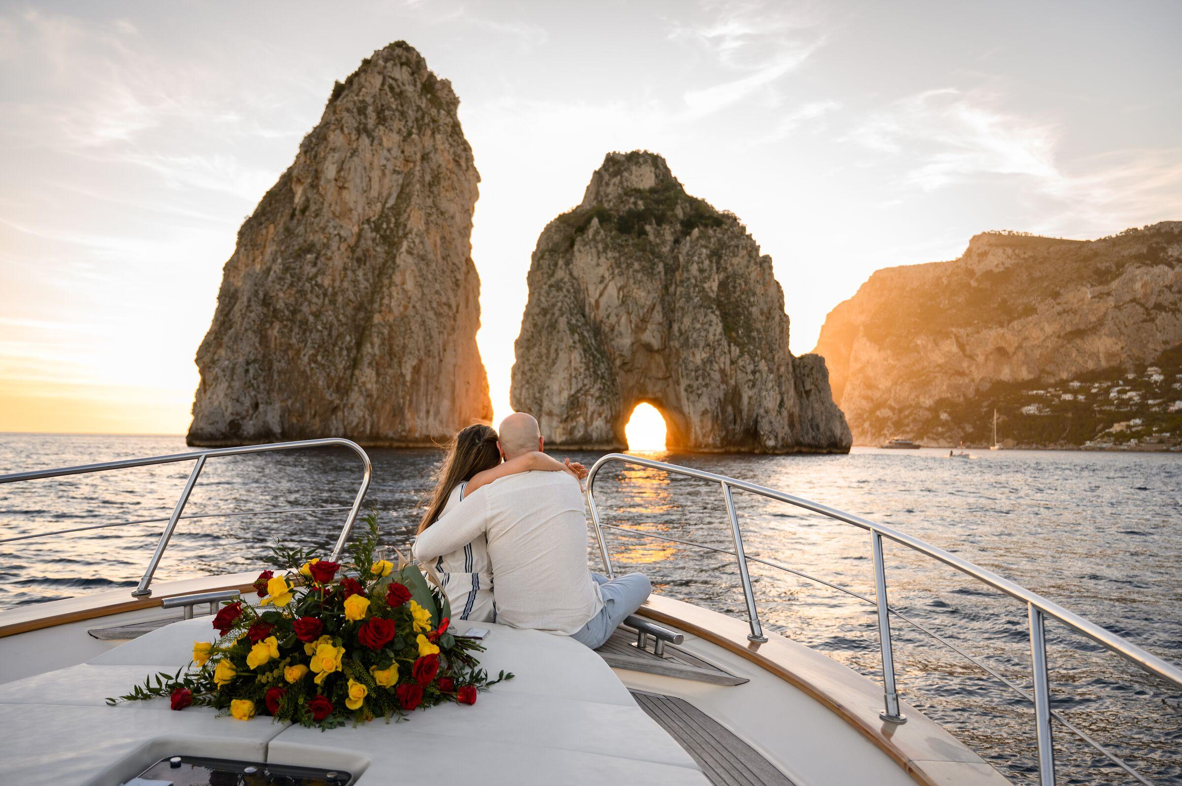 Couple on a yacht bow at sunset, the light through the Faraglioni arch