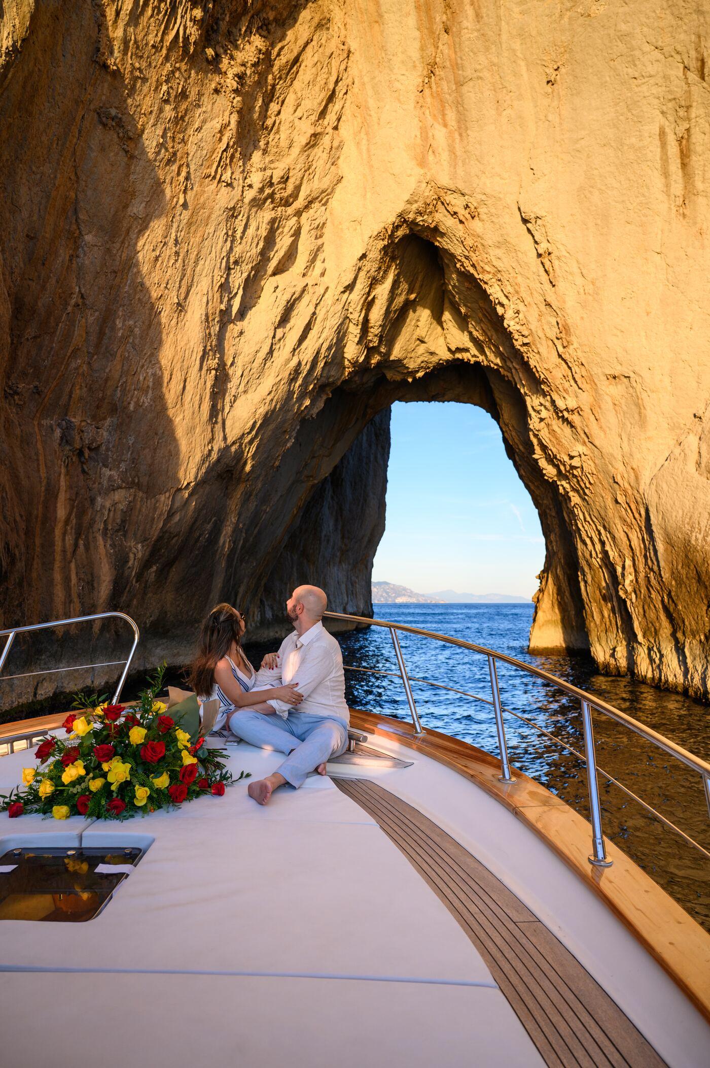 Couple on deck beneath a sea arch off Capri, roses beside them