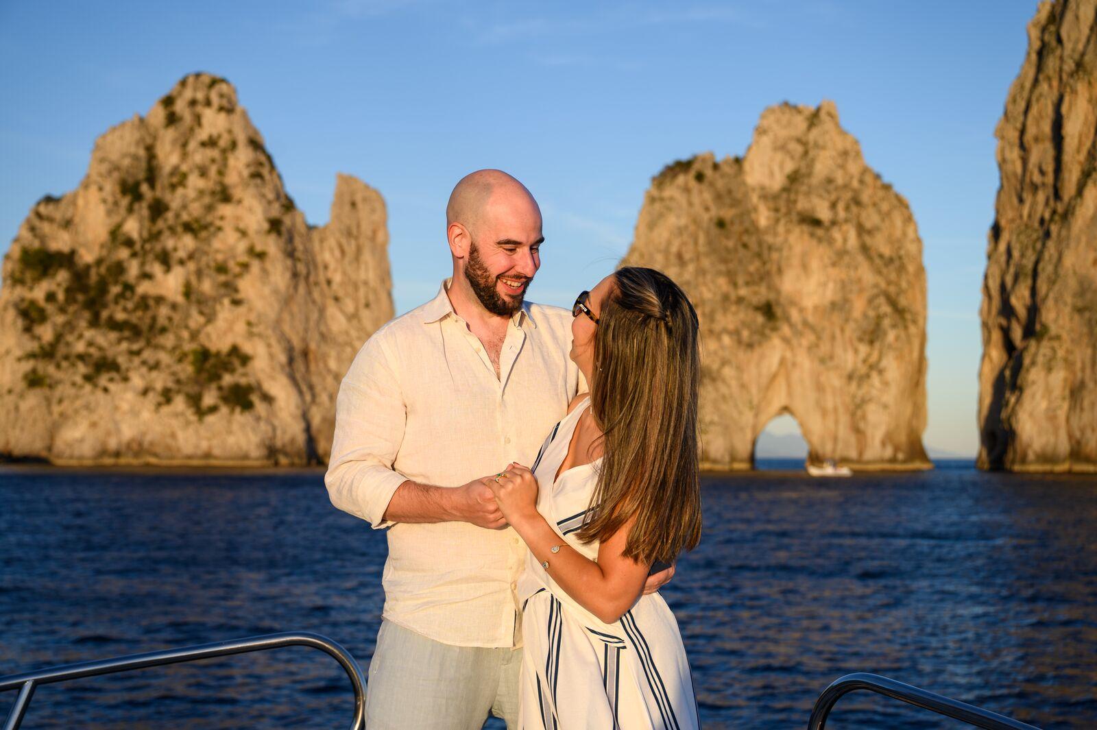 Couple smiling on deck with the Faraglioni behind them
