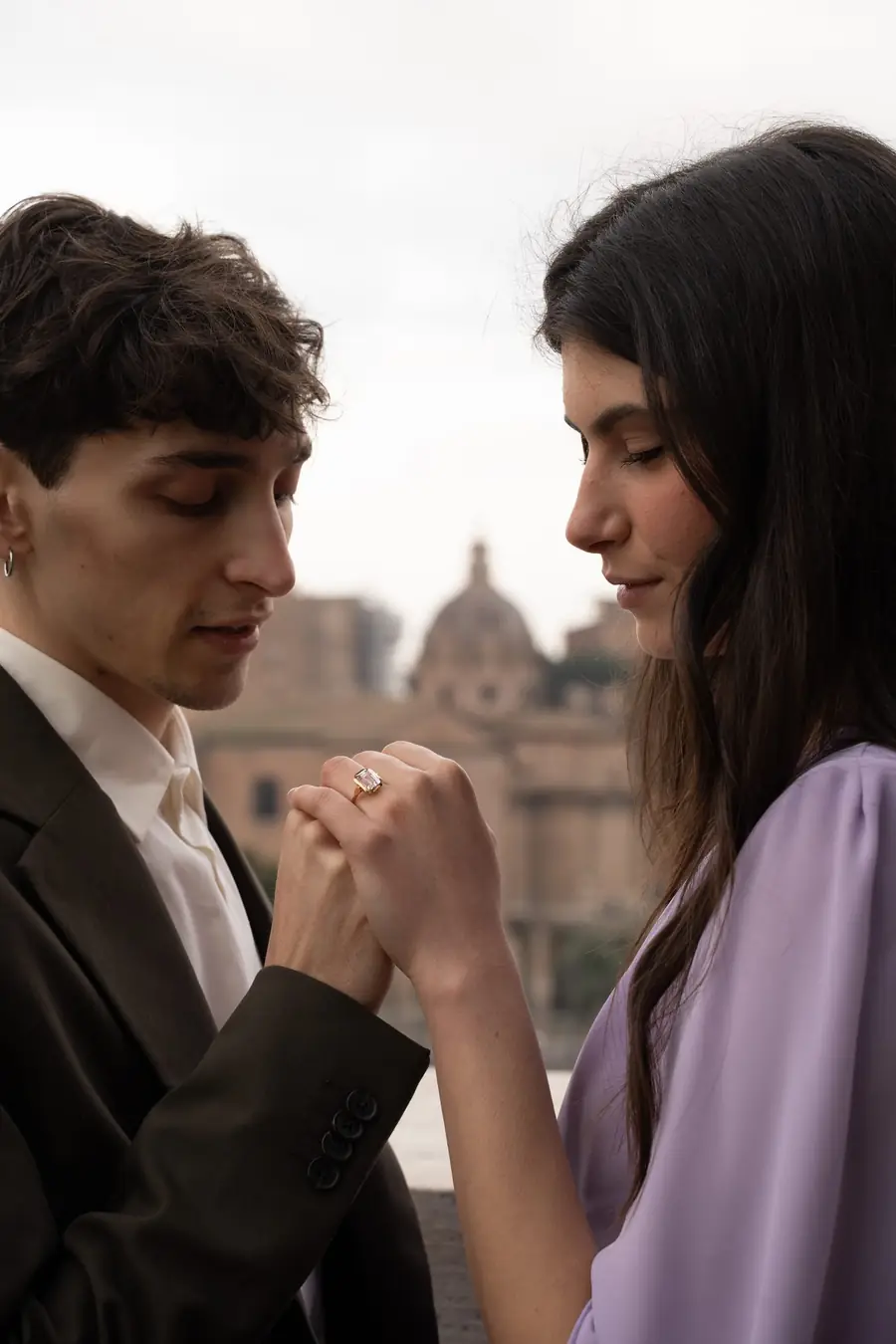 Two hands held close in quiet conversation, Rome's domes softly behind