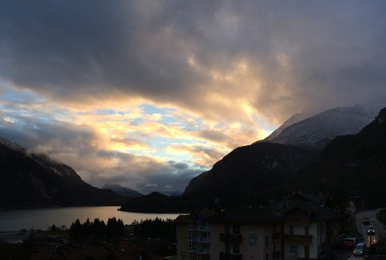 Late light breaking through storm cloud over Lake Molveno, with the first snow of autumn on the mountains above the village