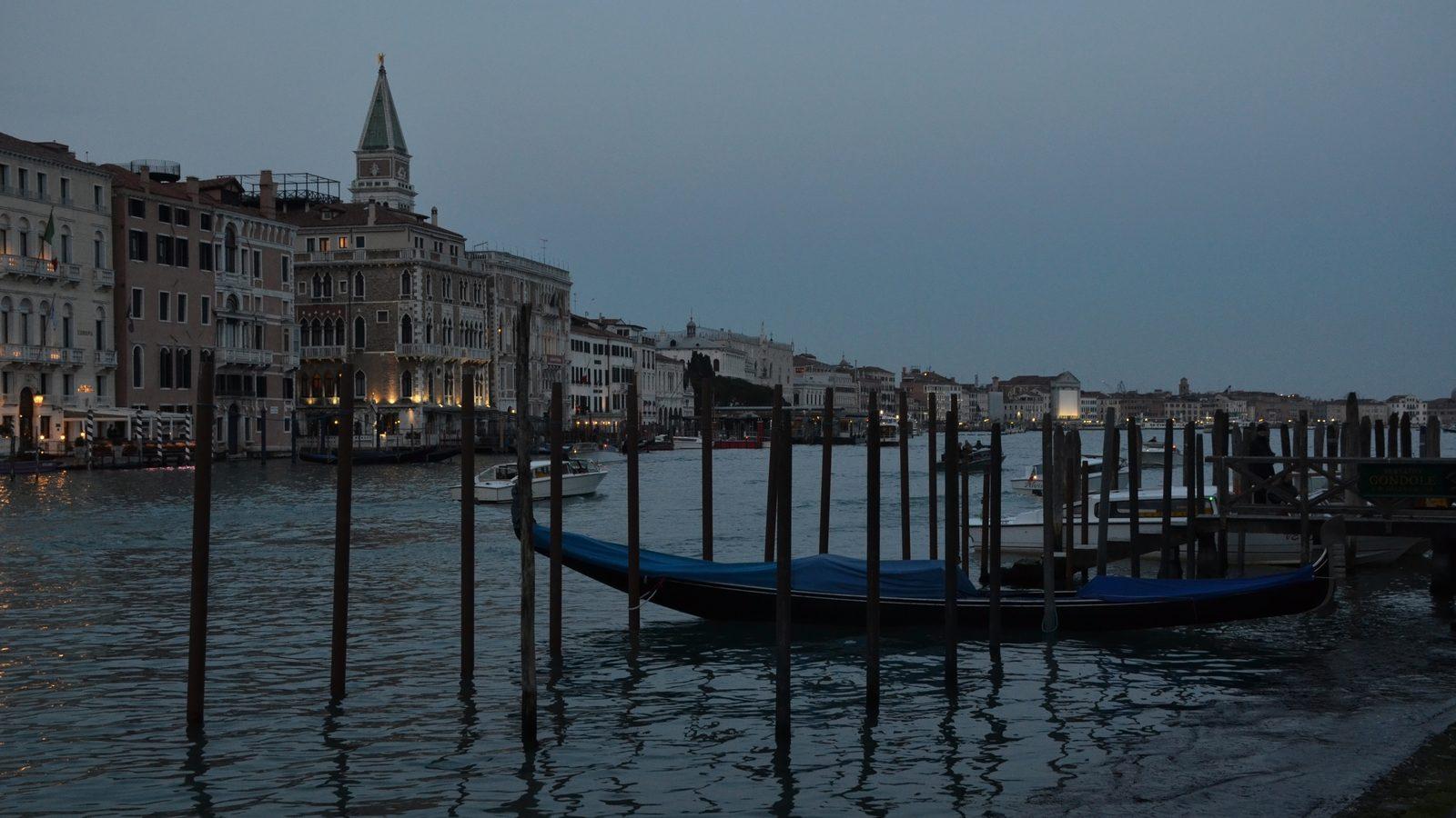A gondola moored on the Grand Canal in Venice at dusk, with the campanile of San Marco behind